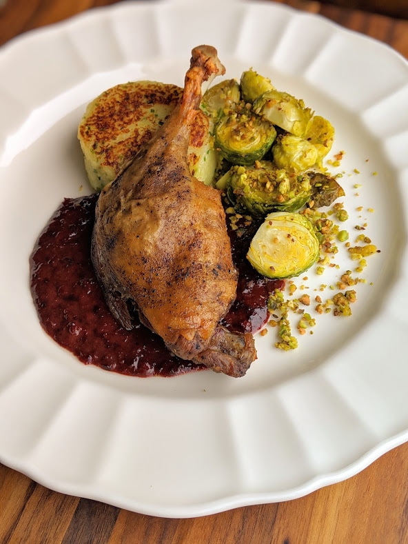 Crispy duck confit leg with sour cherry beurre rouge, chive potato cake and oven roasted Brussel sprouts with pistachios.